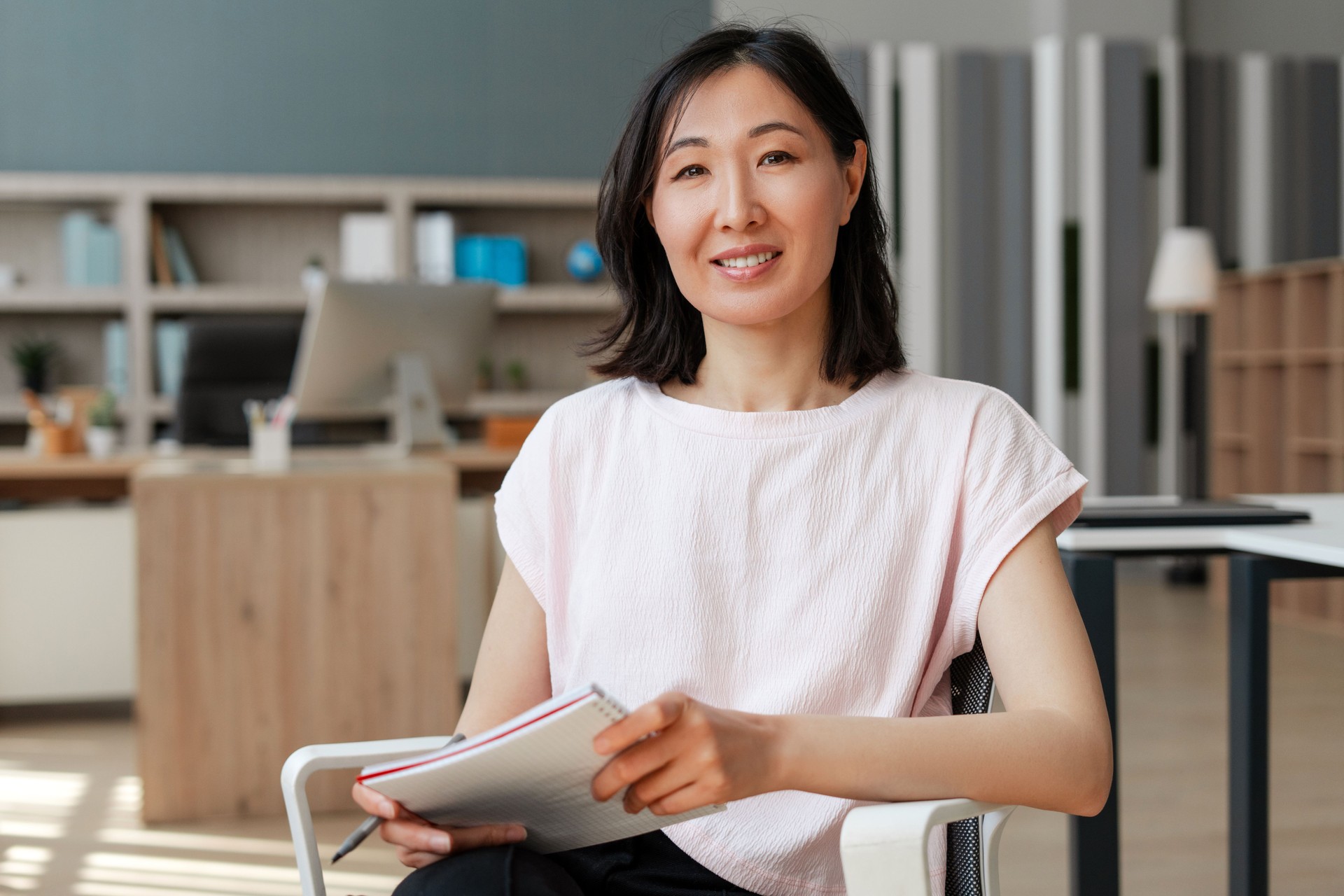 Attractive Asian businesswoman smiling while holding notebook in office