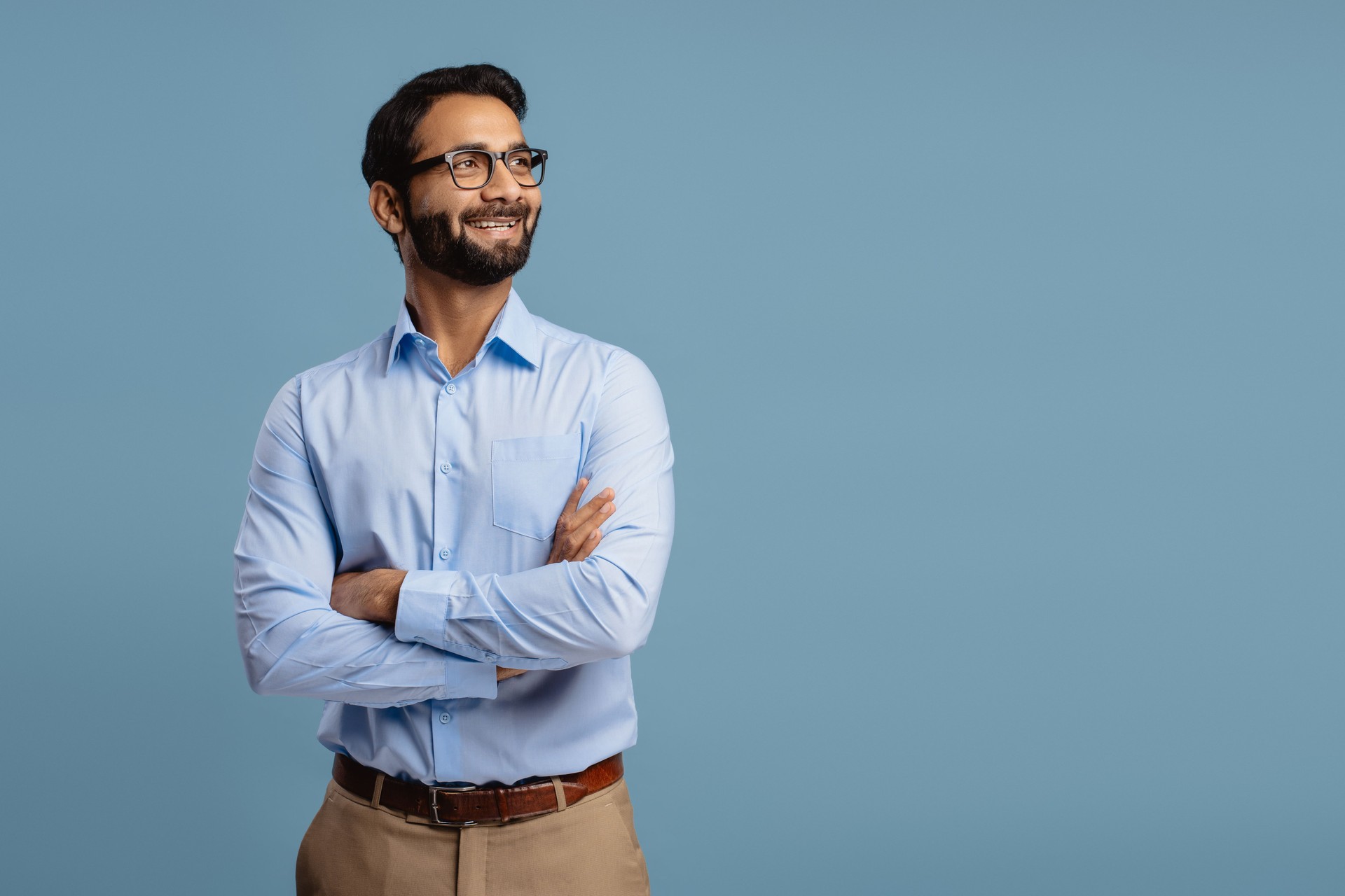 Confident bearded Indian man wearing stylish eyeglasses with crossed arms looking away on copy space